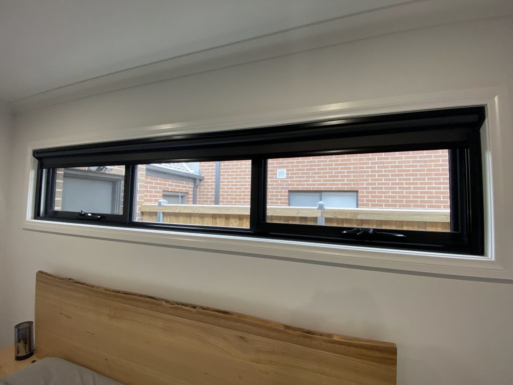 Coverlight blackout blind in satin black over a bedroom window, mounted directly above the bed